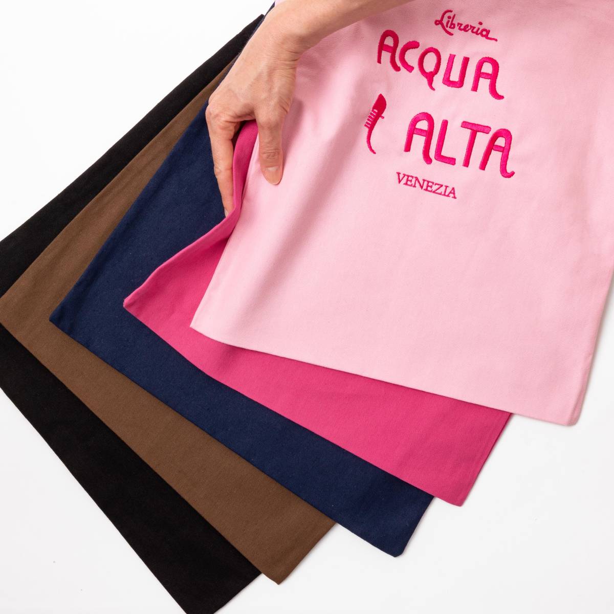 Borsa di tela Libreria Acqua Alta Venezia colore rosa con logo ricamato, tenuta in mano